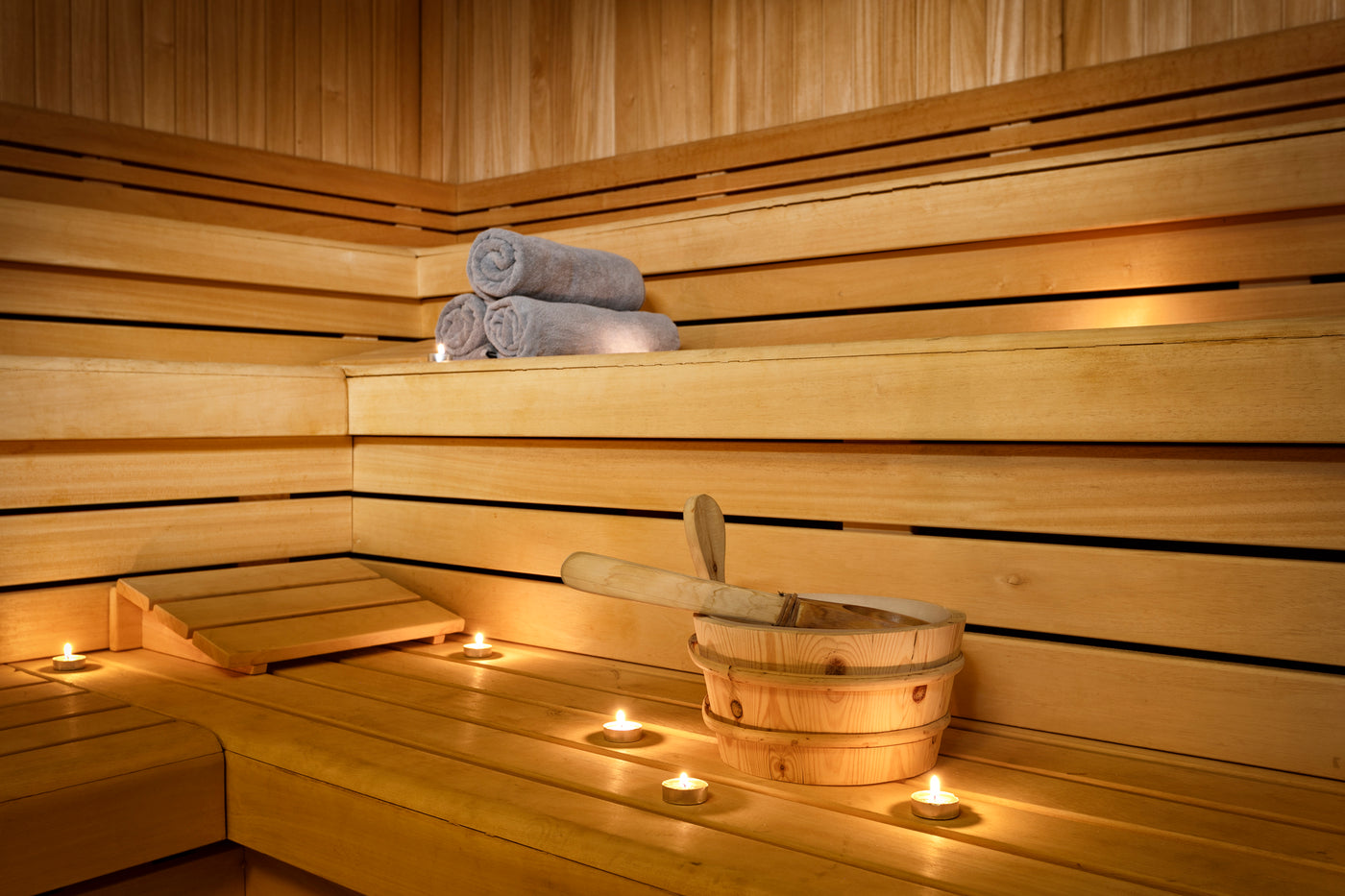 Sauna accessories such as candles, towels and a bucket and ladle are sitting on a sauna bench