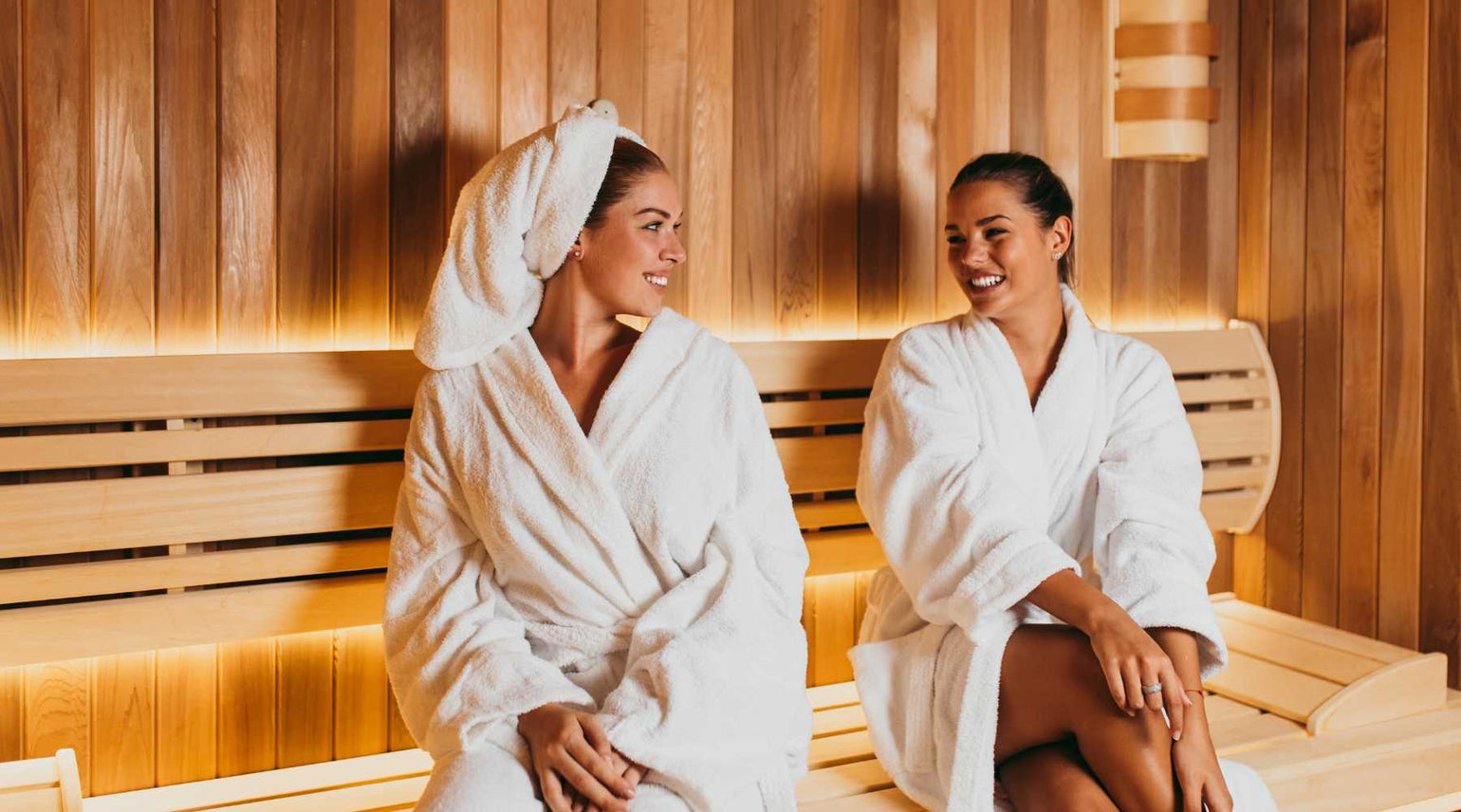 Two woman sitting with bath robes on inside a sauna