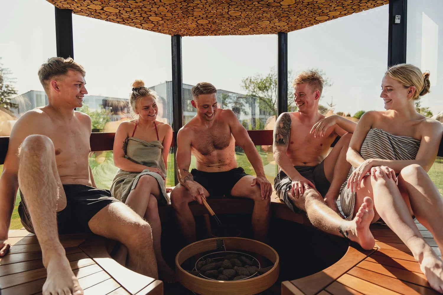 5 people sitting inside an outdoor sauna whilst smiling